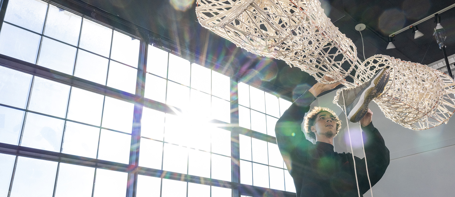 UWM student Mich Dillon adjusts a sculpture made from a basketball shoe and hoop netting as the morning sun shines through the windows in a Kenilworth studio.