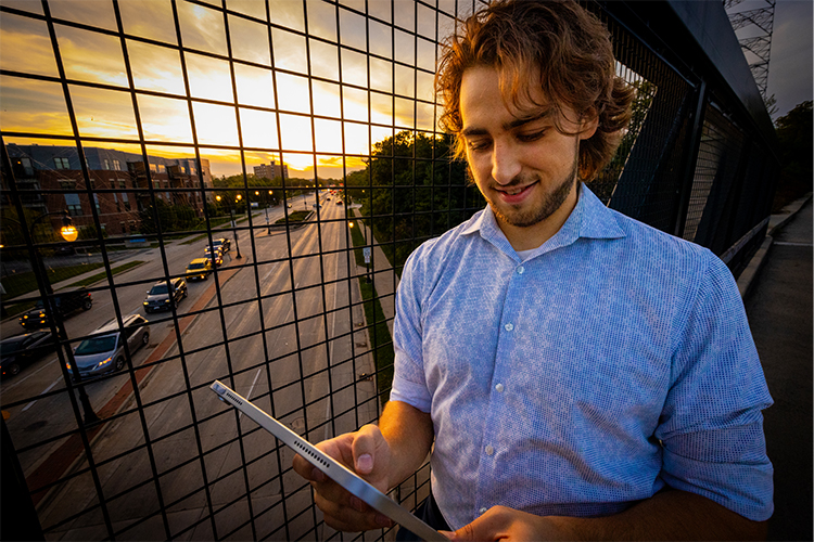 Joel Roberts standing on a bridge over a road and holding holding a tablet device